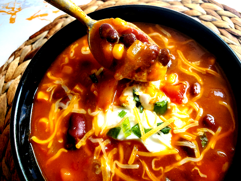 Pumpkin chili in a bowl topped with sour cream and cheese and green onion