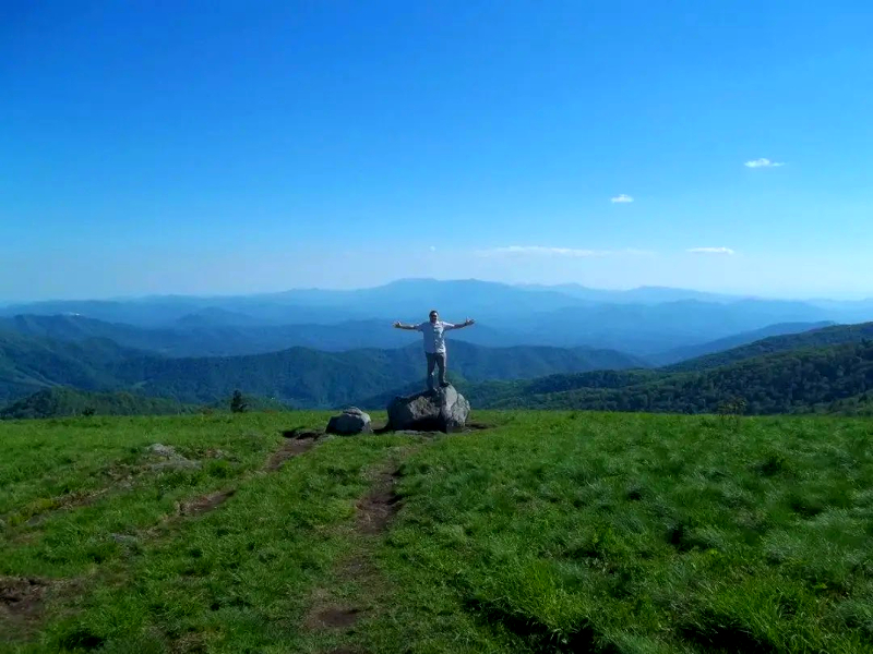 man standing with arms open wide on top of the Roan Highlands