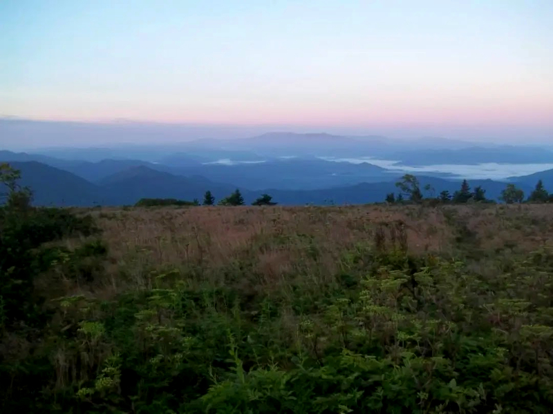 morning on top of a mountain summit with fog below in the valleys